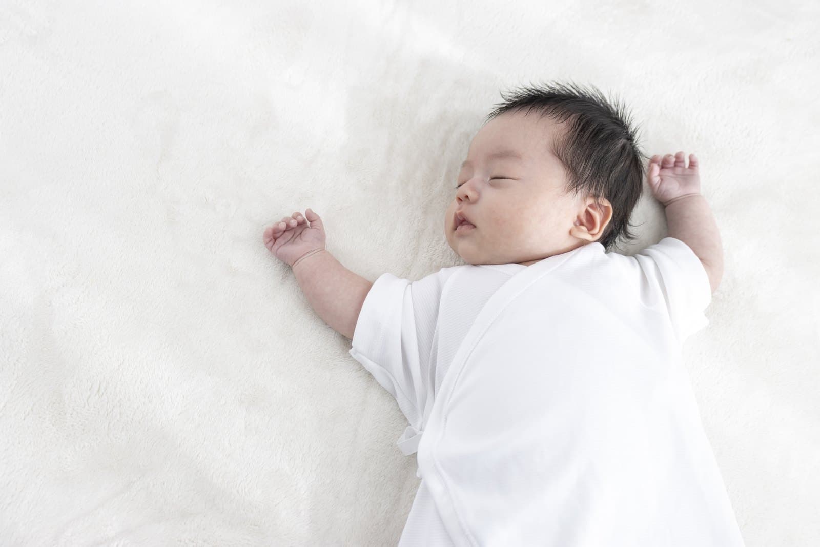 白いシーツの上で、仰向けで静かに眠る赤ちゃん